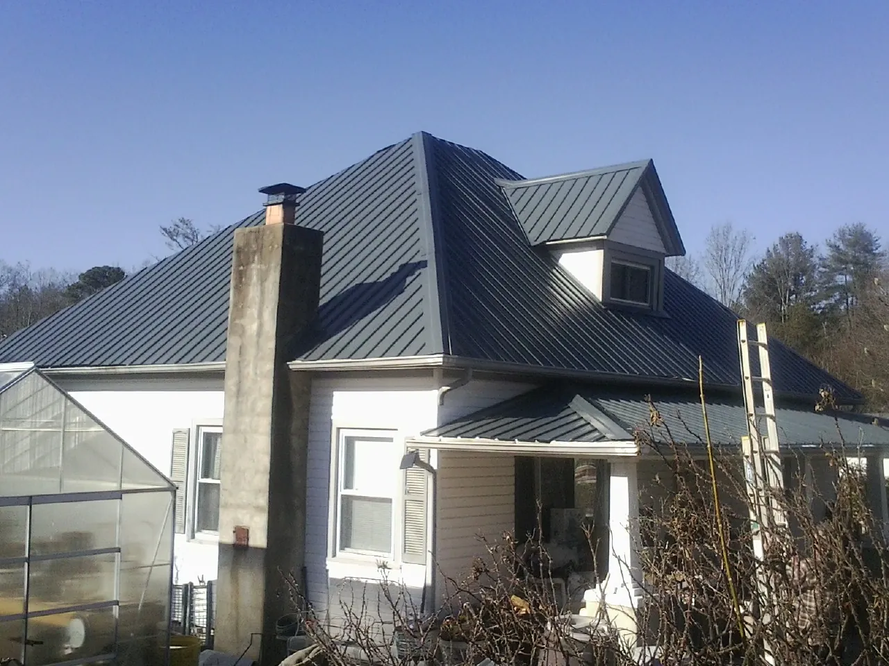 Dark blue standing seam metal roof on a white farmhouse with dormer — Slate & Tile Roof Repair by Roofing Brothers in Mc Farlan