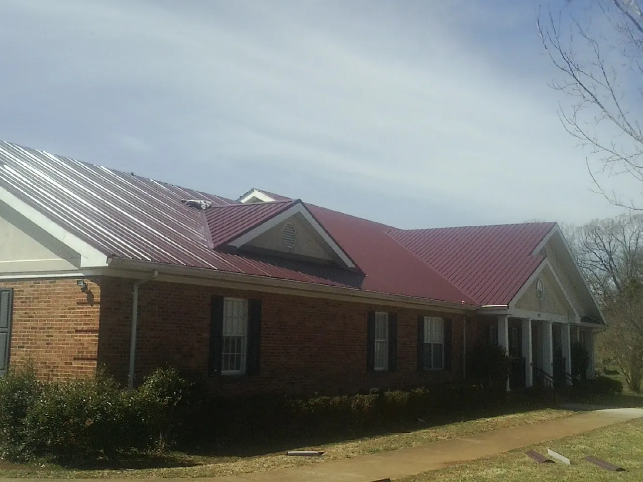 Red metal roof with gabled entries on a long brick building, from a Hail Damage Roof Repair job in Mc Farlan