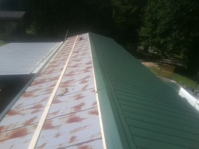 Old rusted panels beside newly installed green metal roofing — Wind Damage Roof Repair by Roofing Brothers in Mc Farlan