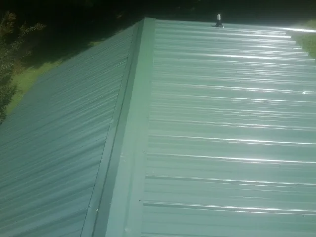 New green metal panels meeting at the ridge of a roof — Flat Roof Repair work by our crew in Mc Farlan