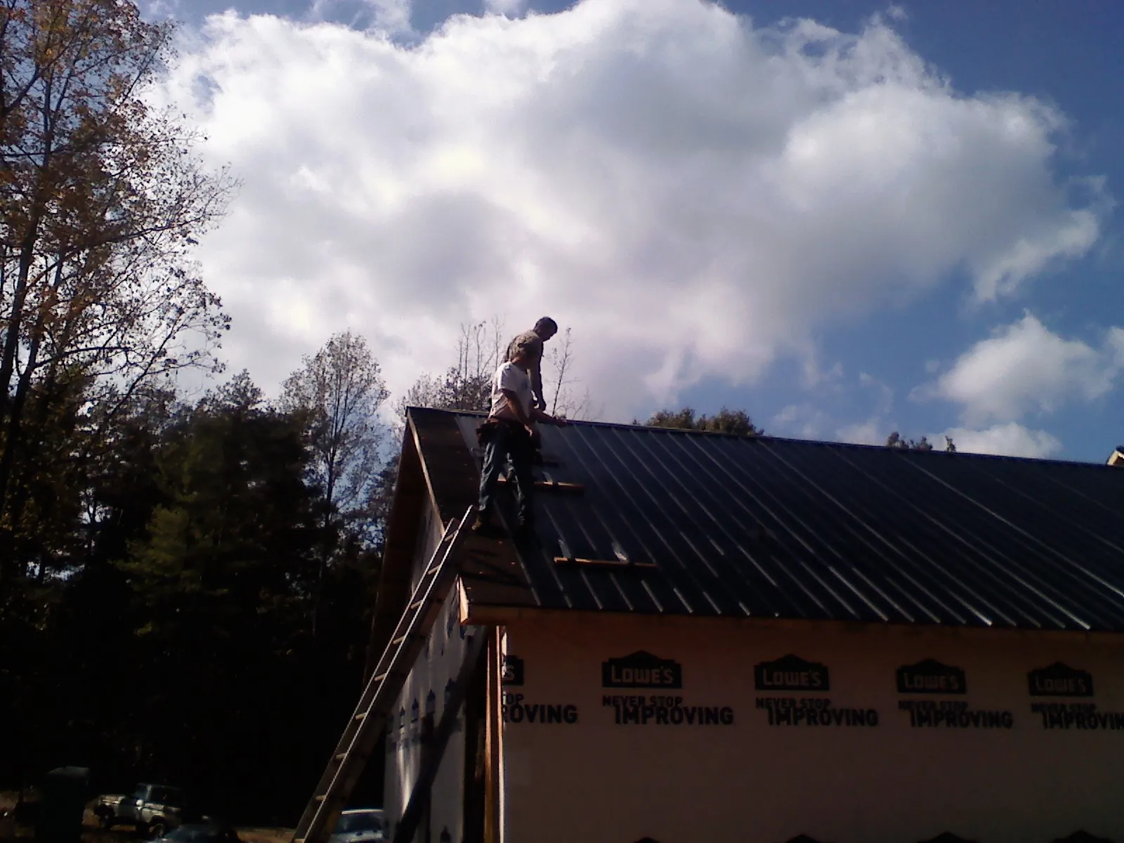 Roofer fastening dark metal panels high against a cloudy sky, from a Roof Inspection job in Mc Farlan