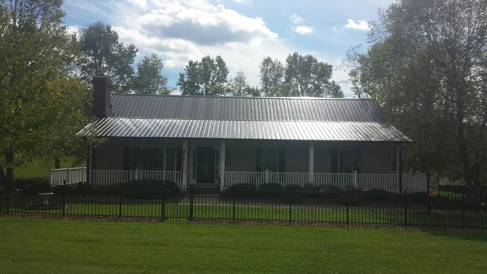 Gray metal roof on a brick ranch with a full width front porch — Gutter Guard Installation work by our crew in Mc Farlan