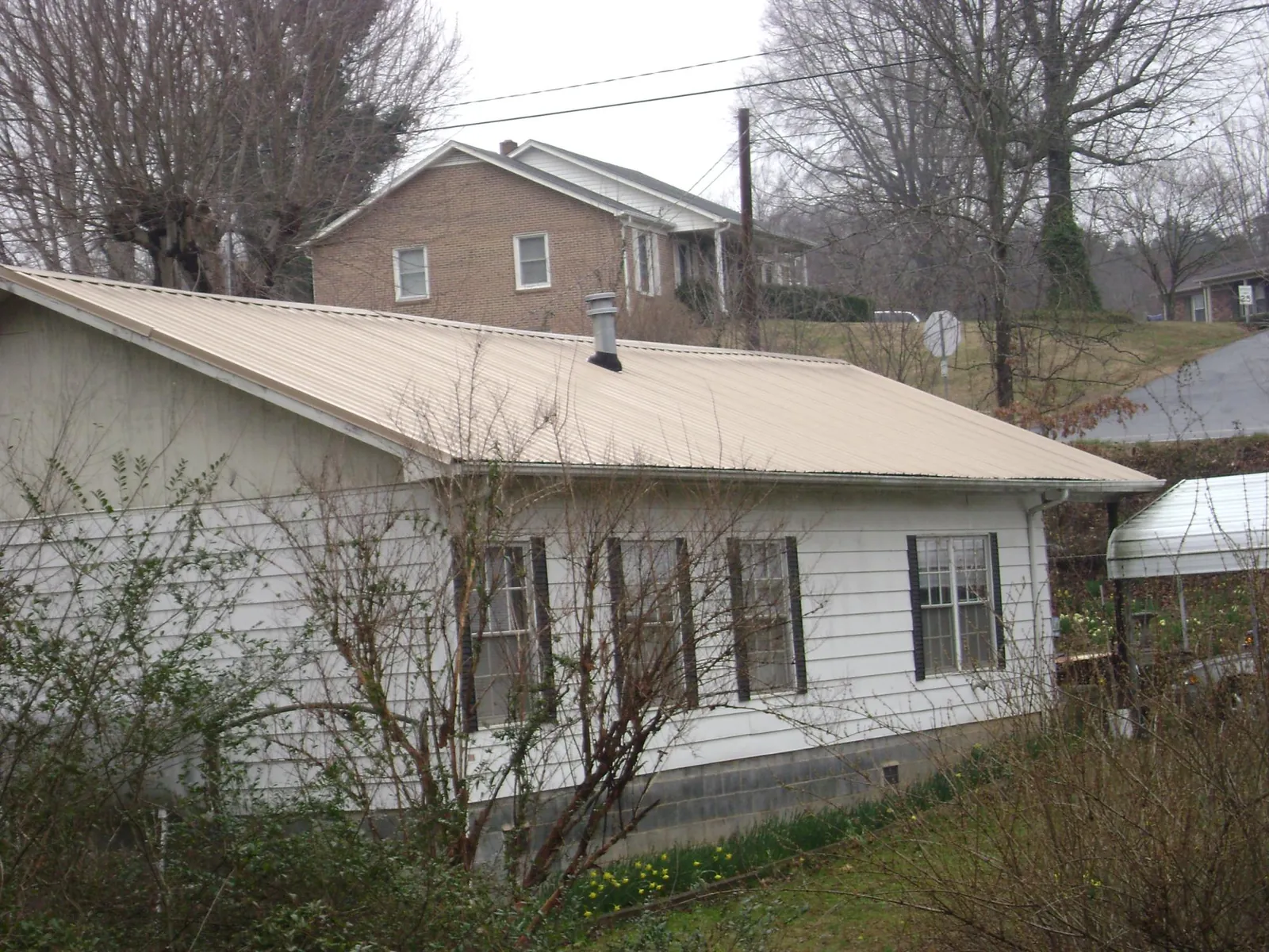 Tan metal roof on a white sided house set into a hillside — Commercial Roofing by Roofing Brothers in Mc Farlan