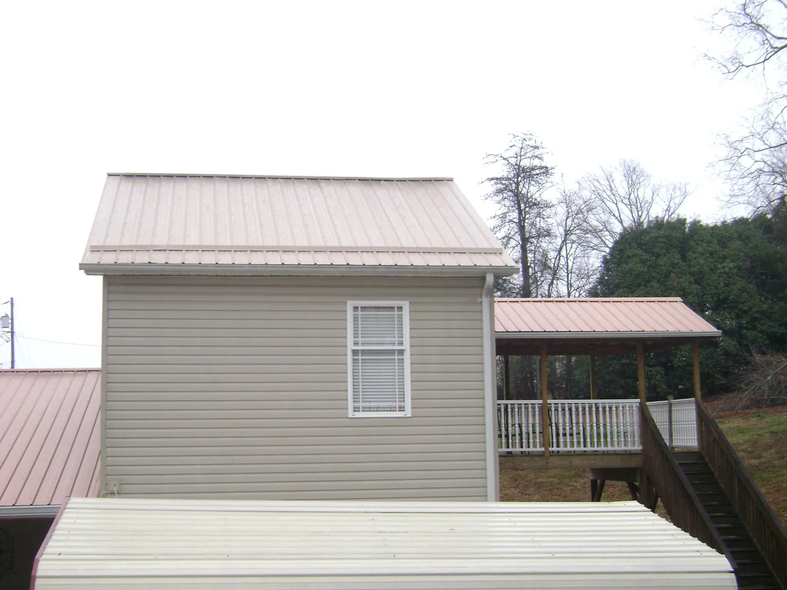 Tan metal roofs on a two story addition and attached porch, from a Roof Replacement job in Mc Farlan